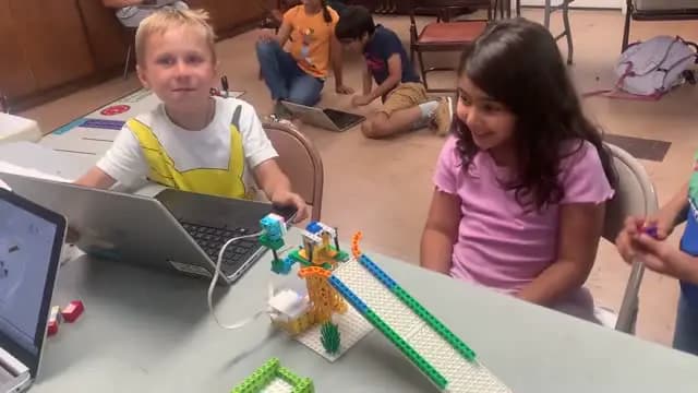 Two campers laughing while building a LEGO robot